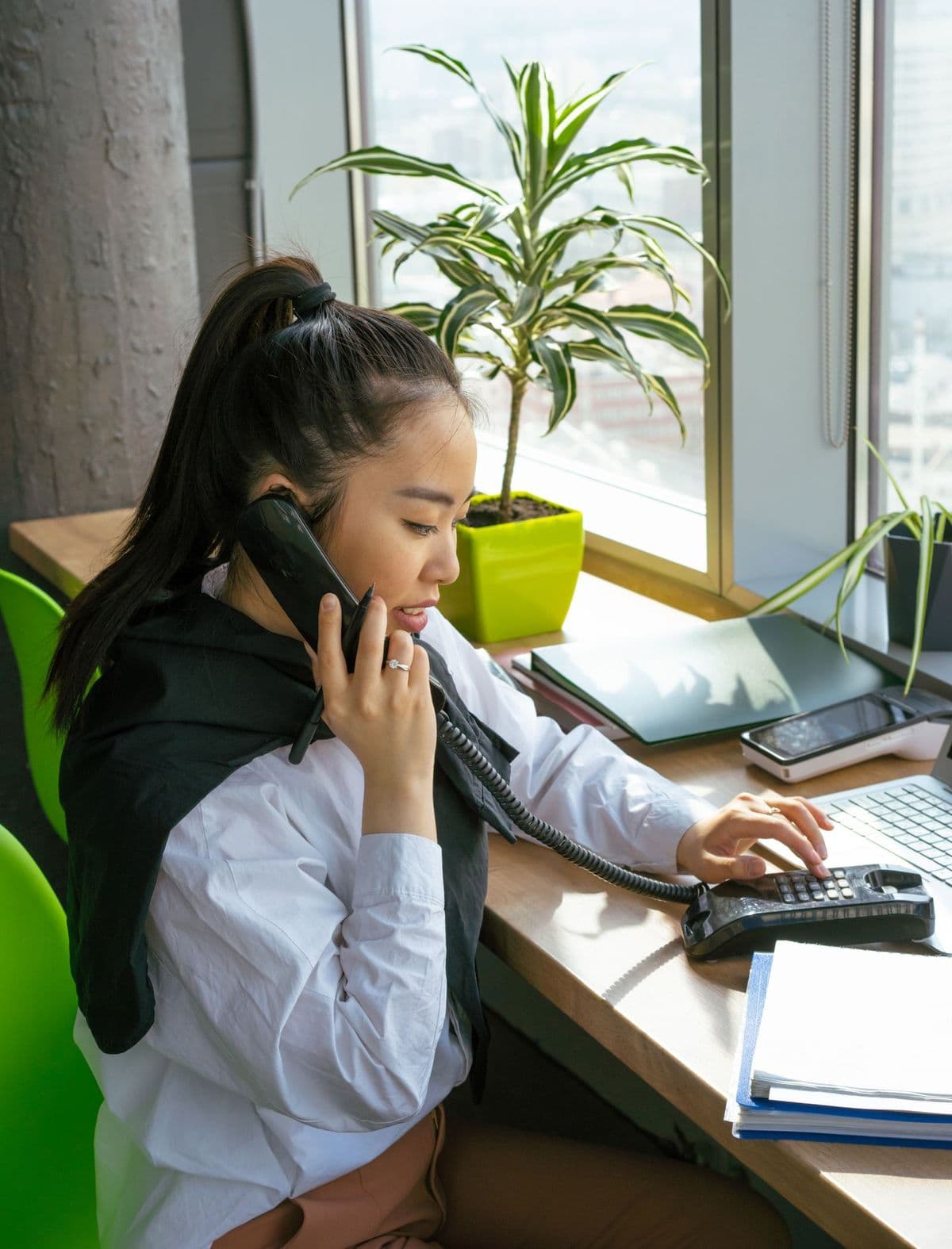 Profissional de RH ao telefone, com o notebook e as pastas sobre a mesa.